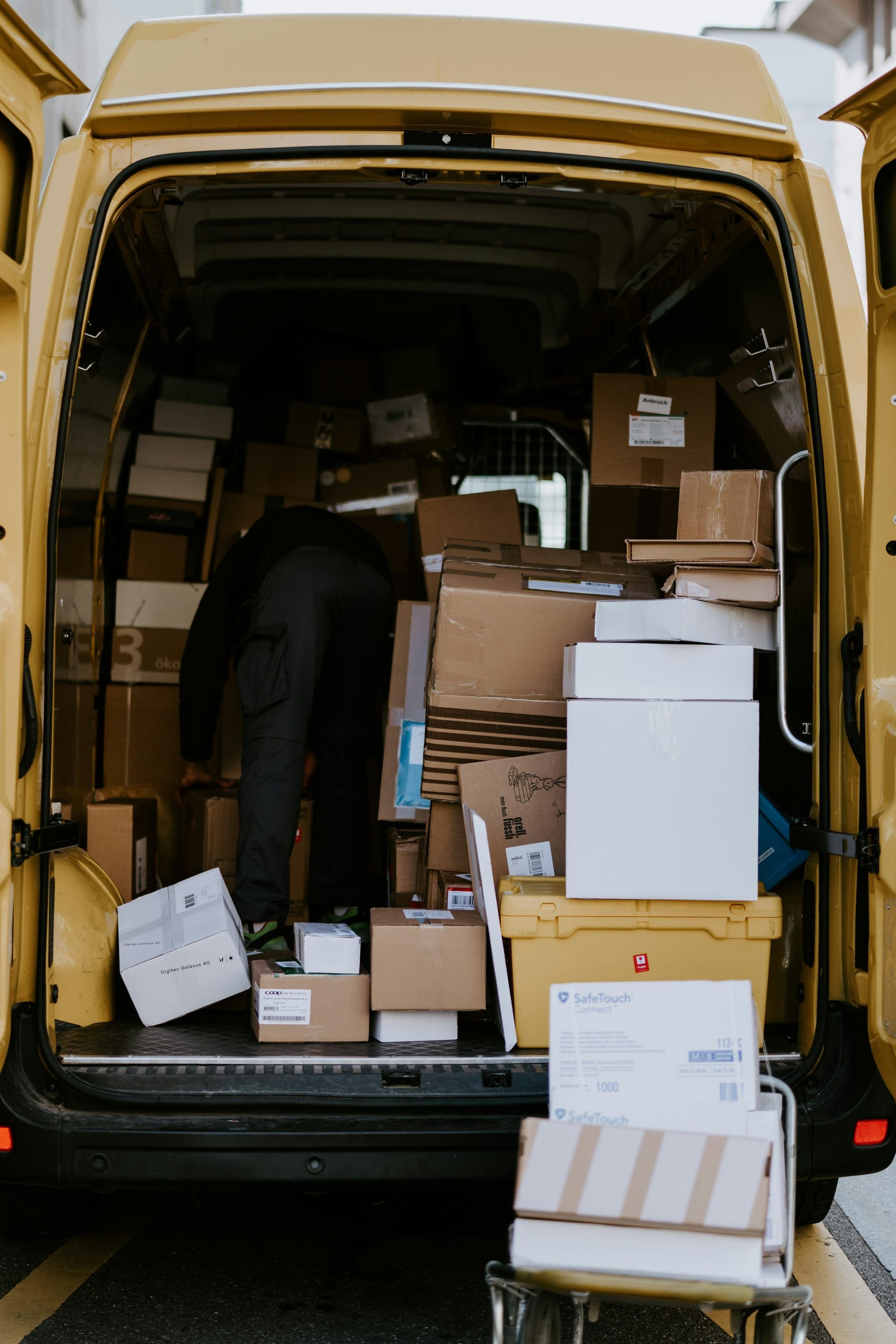 A courier loading cardboard boxes into a delivery van