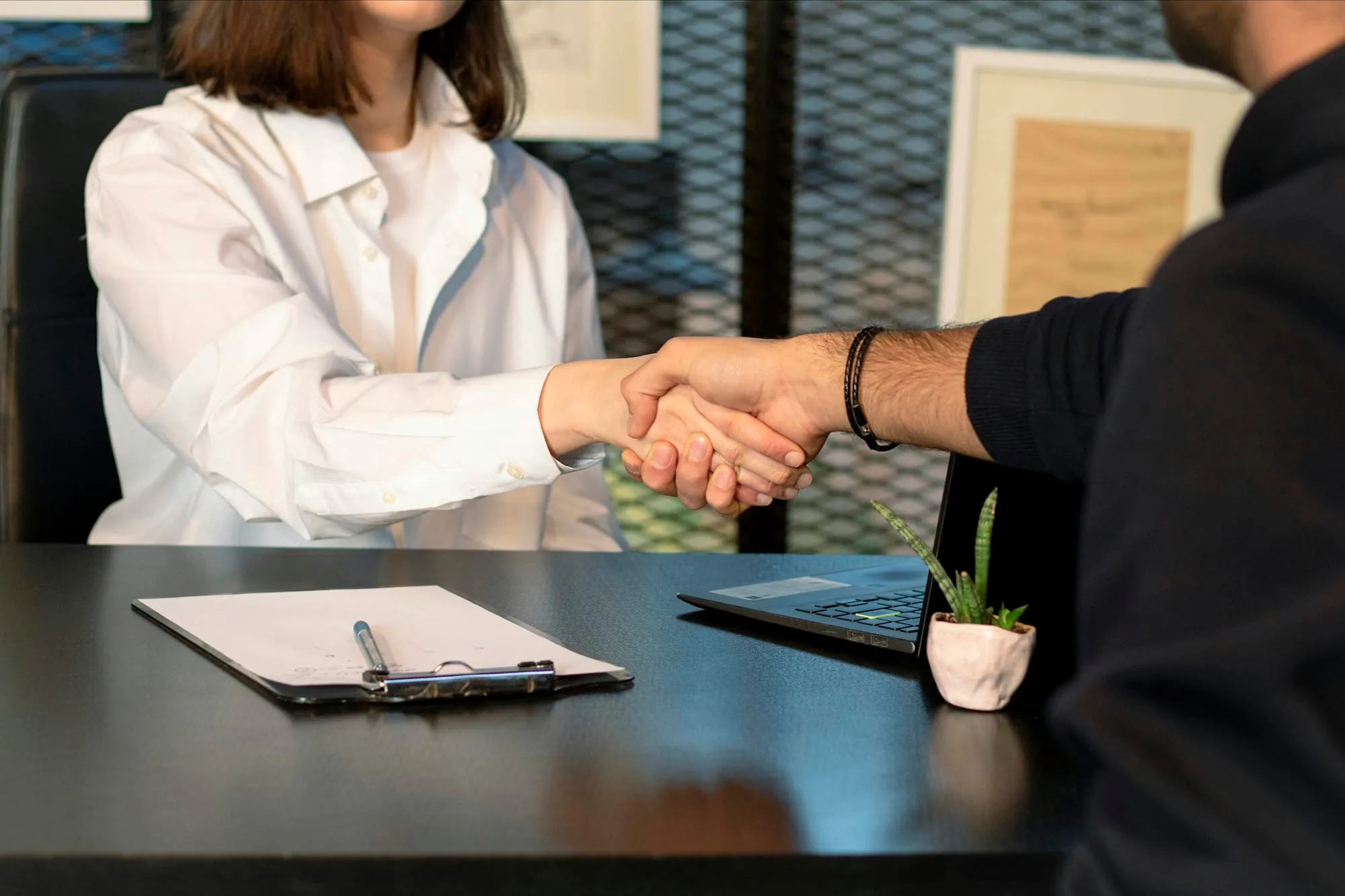 Two people shaking hands over a desk with a signed contract